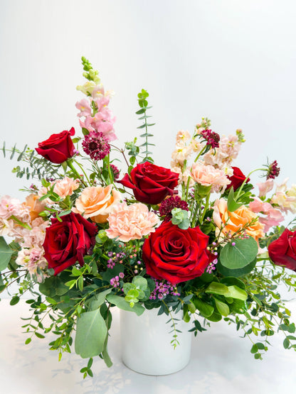 Bouquet of red, peach, and pink flowers in a white vase on a light background